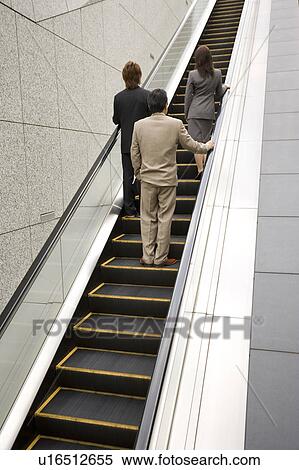 Three business people ascending escalator View Large Photo Image Stock Photography - Three business people ascending escalator. Fotosearch