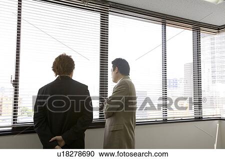 Stock Image - Two people looking through blinds. Fotosearch