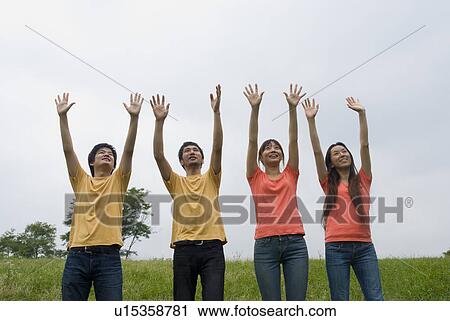 Stock Image - Four people standing with arms raised. Fotosearch