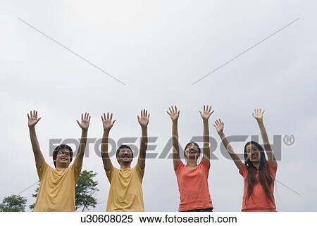 Four people standing with arms raised View Large Photo Image Stock Photography - Four people standing with arms raised. Fotosearch
