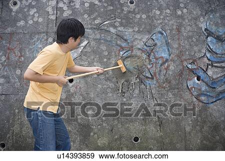 Stock Photo - Young man cleaning graffiti on wall. Fotosearch