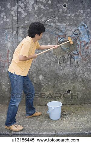 Stock Photography - Young man cleaning graffiti on wall. Fotosearch