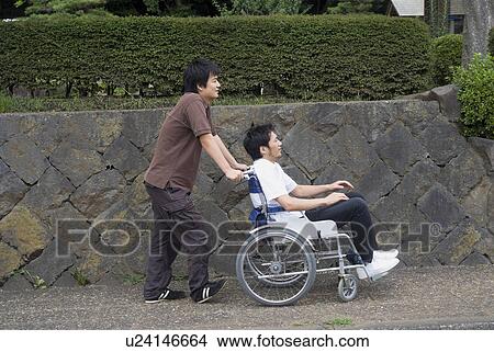 Picture - Young man pushing man on wheelchair. Fotosearch