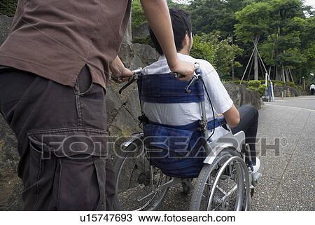 Young man pushing man on wheelchair View Large Photo Image Stock Image - Young man pushing man on wheelchair. Fotosearch