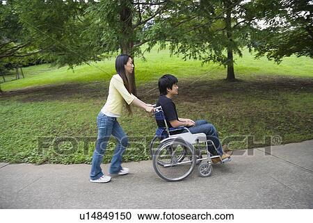 Young woman pushing man on wheelchair View Large Photo Image Stock Image - Young woman pushing man on wheelchair. Fotosearch