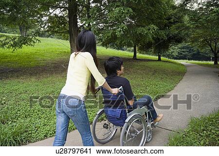 Young woman pushing man on wheelchair View Large Photo Image Stock Image - Young woman pushing man on wheelchair. Fotosearch