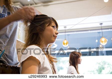 Stock Image - Hairdresser styling young woman's hair. Fotosearch