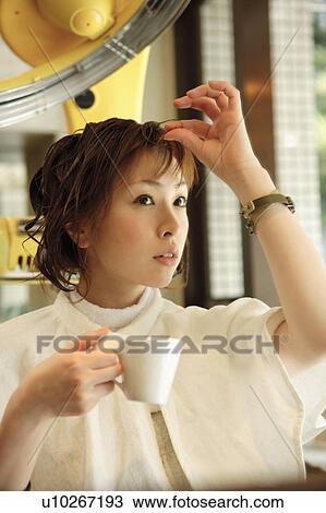 Stock Image - Young woman drinking coffee in hair salon. Fotosearch