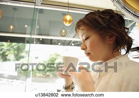 Stock Image - Young woman drinking coffee in hair salon. Fotosearch