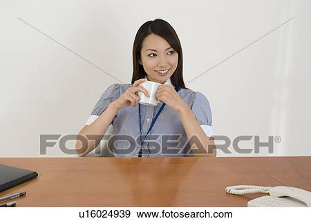Young woman drinking coffee in office View Large Photo Image Stock Photo - Young woman drinking coffee in office. Fotosearch