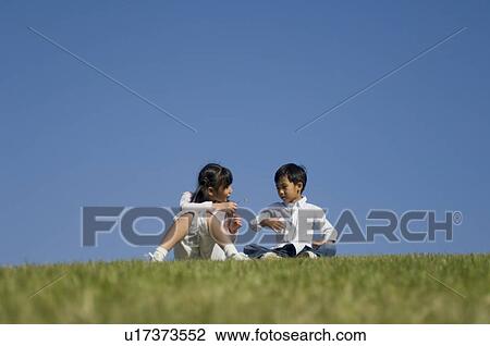 Stock Image - Boy and girl sitting in field. Fotosearch
