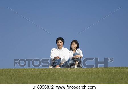 Stock Image - Mid adult couple sitting in field. Fotosearch