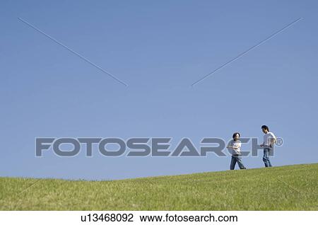 Stock Image - Mid adult couple walking in field. Fotosearch