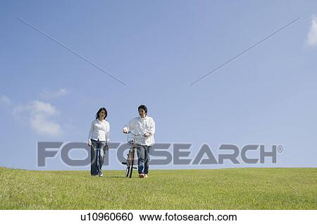 Mid adult couple walking with bicycle View Large Photo Image Stock Image - Mid adult couple walking with bicycle. Fotosearch