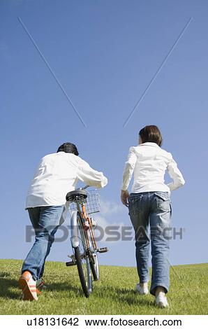 Stock Image - Mid adult couple walking with bicycle. Fotosearch
