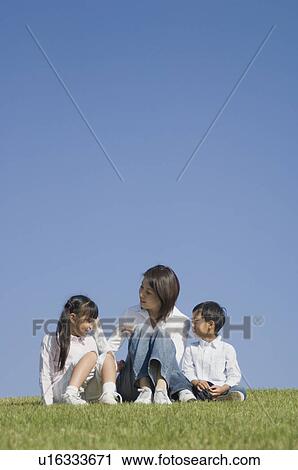 Stock Image - Mother and two children sitting in field. Fotosearch