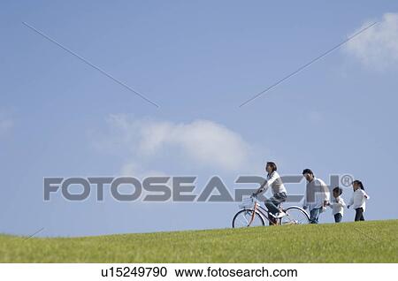 Stock Image - Mother riding bicycle while father and children walking. Fotosearch