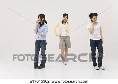 Stock Image - Three young women talking over mobile phones. Fotosearch