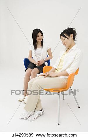 Two young women sitting in chairs View Large Photo Image Stock Photo - Two young women sitting in chairs. Fotosearch