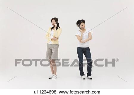 Stock Photo - Two young women talking over mobile phones. Fotosearch