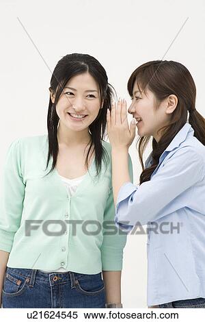 Stock Photography - Young woman whispering to her friend. Fotosearch