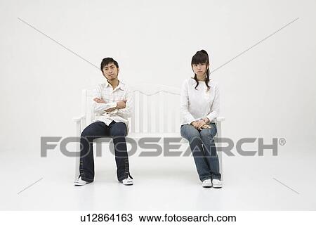 Stock Image - Young couple sitting on bench. Fotosearch