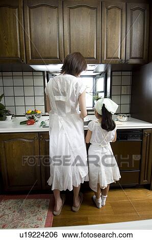 Stock Photograph - Mother and daughter standing in kitchen. Fotosearch
