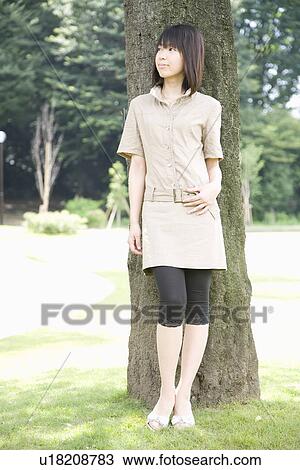 Stock Image - Young woman standing in park. Fotosearch