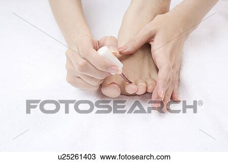 Stock Image - Young woman painting manicure on toenails. Fotosearch