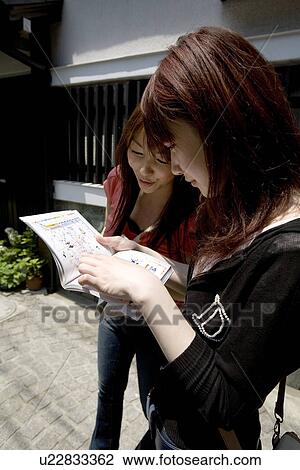 Stock Image - Two women looking at guidebook. Fotosearch