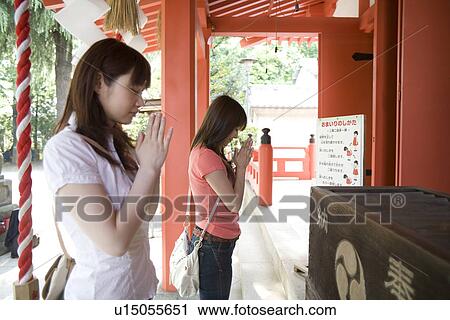 Stock Image - Two young women praying at shinto shrine. Fotosearch