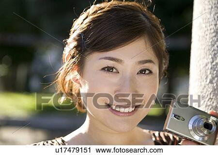 Stock Image - Young woman holding digital camera. Fotosearch