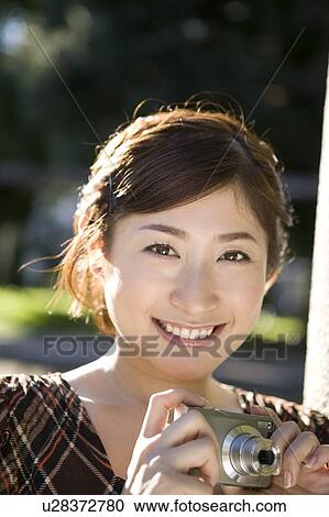 Stock Image - Young woman holding digital camera. Fotosearch