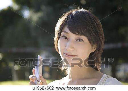 Stock Image - Young woman holding mobile phone. Fotosearch