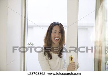 Stock Image - Young woman opening door. Fotosearch