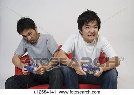 Stock Image - Two young men playing video game. Fotosearch
