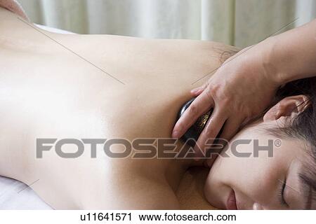 Stock Image - Young woman receiving stone massage. Fotosearch
