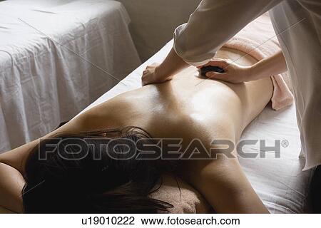 Stock Image - Young woman receiving stone massage. Fotosearch