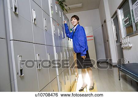 Stock Photograph - Young woman standing in front of locker. Fotosearch