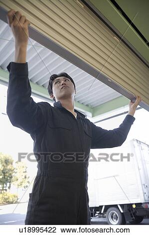 Stock Image - Young workman opening shutter of warehouse. Fotosearch