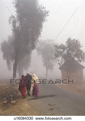 Stock Image - Three people walking along foggy road - Napel. Fotosearch
