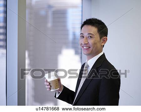 Businessman holding coffee standing by window, smiling View Large Photo Image Stock Photo - Businessman holding coffee standing by window, smiling. Fotosearch