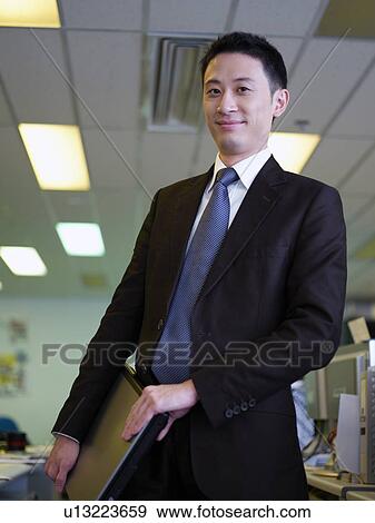 Stock Photo - Businessman holding laptop, smiling, portrait. Fotosearch