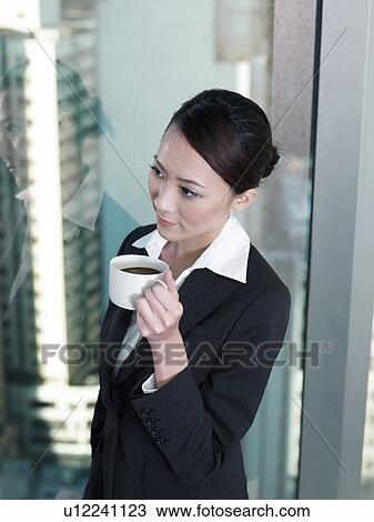 Businesswoman holding a cup of coffee standing by window View Large Photo Image Stock Image - Businesswoman holding a cup of coffee standing by window. Fotosearch