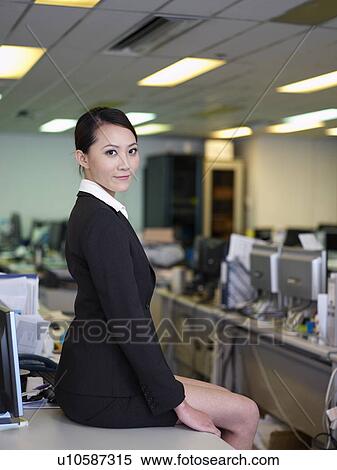Stock Photography - Businesswoman sitting on desk in offiice. Fotosearch