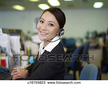 Stock Image - Businesswoman wearing headset in office, smiling. Fotosearch