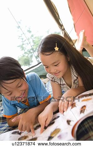 Picture - Boy and girl lying down and looking at encyclopedia. Fotosearch