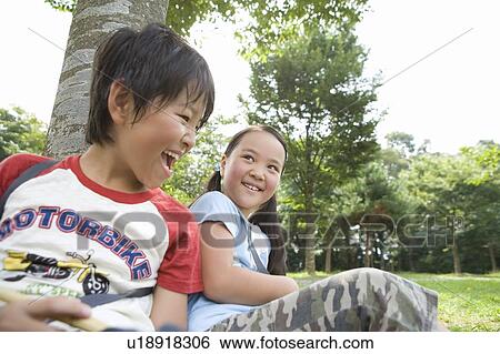 Stock Photograph - Boy and girl sitting against tree. Fotosearch