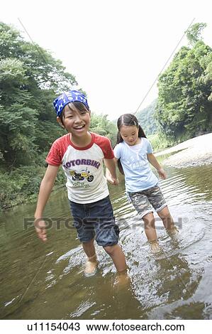 Stock Image - Boy and girl walking in stream, holding hands. Fotosearch