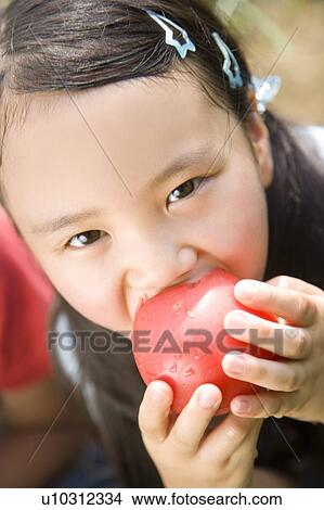 Picture - Close up of a girl biting tomato. Fotosearch